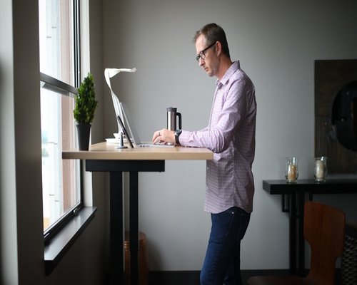 An individual standing and stretching hands moderately beside a bright office window